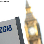 An NHS sign at St Thomas' Hospital, with Big Ben in the background, in Westminster, central London